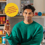 Man in kitchen holds Diaspora Spices Co. - Hawaij Masala tin, with shelves of spices visible, highlighting collaboration with cultural icon Nadir Nahdi.