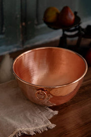 Coppermill Kitchen LLC - Coppermill Vintage Inspired Mixing Bowl on a wooden surface, featuring a hammered-copper design with a ring handle and a lace-trimmed linen cloth.