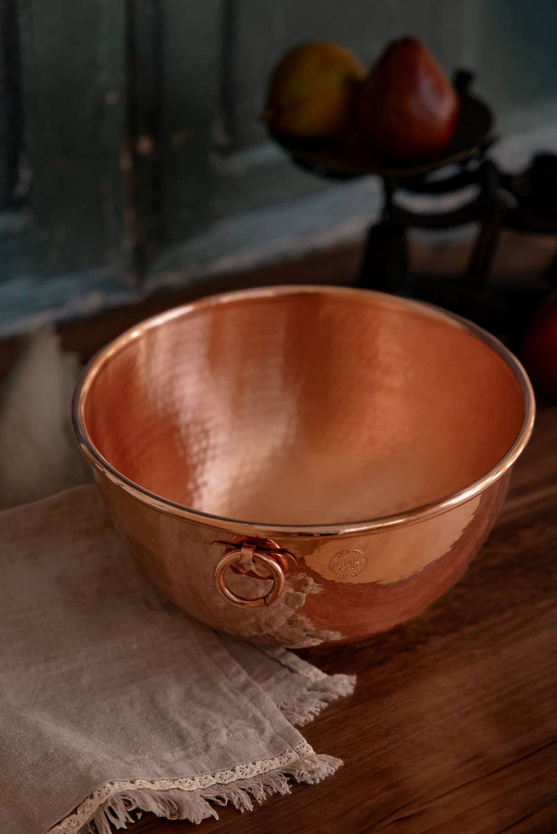 Coppermill Kitchen LLC - Coppermill Vintage Inspired Mixing Bowl on a wooden surface, featuring a hammered-copper design with a ring handle and a lace-trimmed linen cloth.