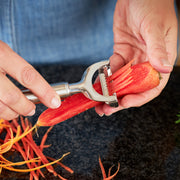 Hands using Rösle | Peelers - Julienne on a carrot, producing thin strips. Ideal for slender vegetables, suitable for all users, with a replaceable, serrated blade.