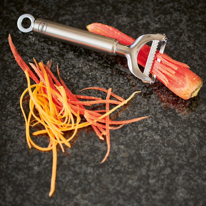Rösle | Peelers - Julienne slicing a carrot into thin strips, showcasing its efficiency on a dark countertop. Ideal for slender vegetables, suitable for both-handed use.
