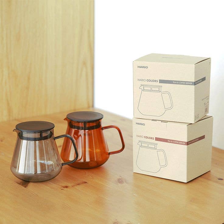 HARIO USA - HARIO Colors Glass Coffee and Tea Server, 600ml: Amber, with mesh filter lid, shown alongside packaging on a wooden table.