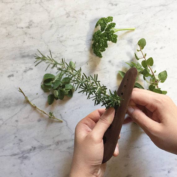 Collin Garrity - Herb Stripper: Cherry used to strip rosemary leaves, surrounded by fresh herb sprigs; versatile tool for efficient herb preparation.