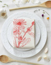 Hearth and Harrow - Organic Cotton Calendula Tea Towel in Red displayed on a white plate with spoons, showcasing its floral print and kitchen utility.