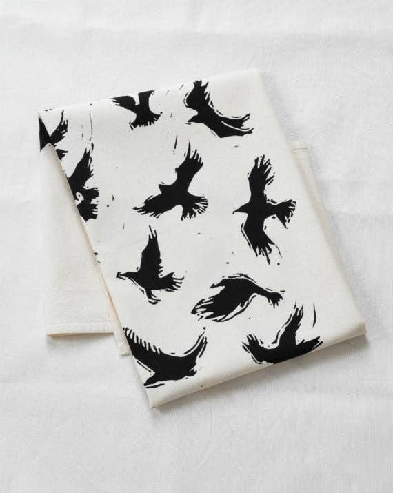 Hearth and Harrow Organic Cotton Flying Crows Tea Towel, featuring black raven silhouettes on off-white fabric, hand-printed with eco-friendly ink and a twill hanging loop.