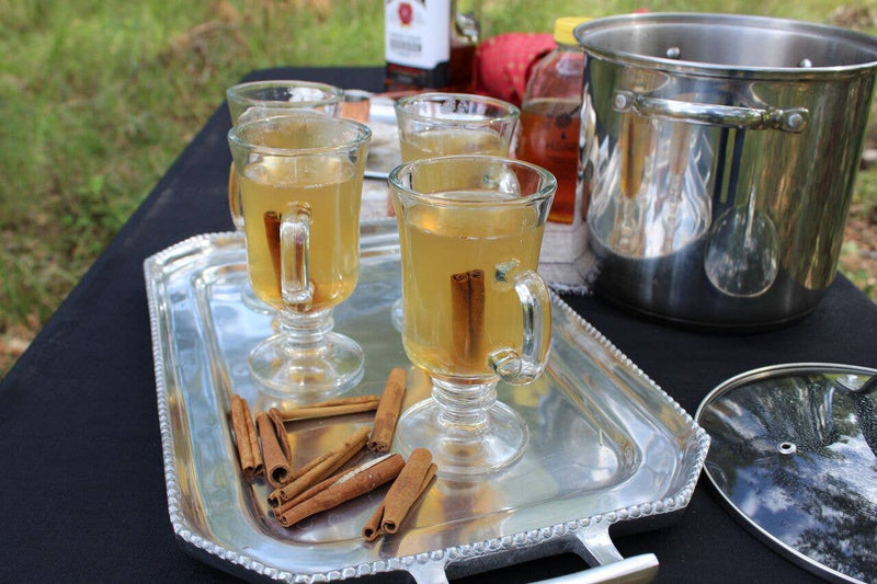 Oliver Pluff & Company - Orange Clove Hot Toddy Kit with clear glass mugs, cinnamon sticks, and a stainless-steel pot, evoking a warm, spiced drink experience.