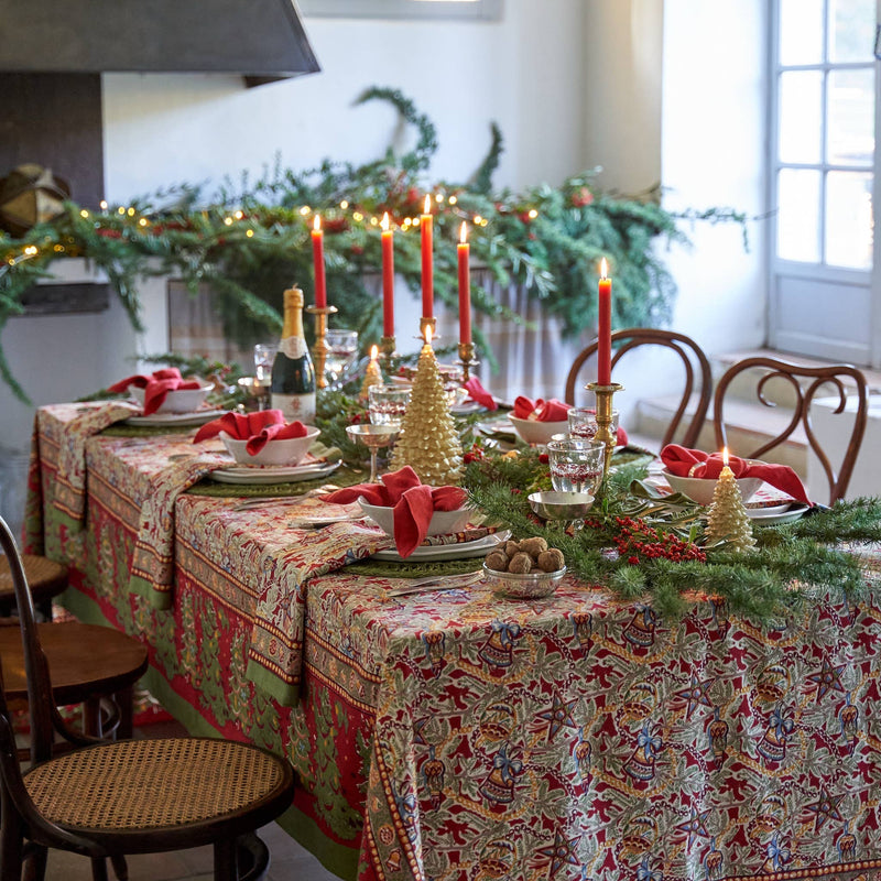Couleur Nature - Noel Red & Green Tablecloth elegantly adorns a festively set dining table with pine garland, candles, and tableware, reflecting holiday charm.
