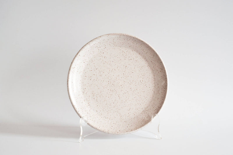 RachaelPots - Salad Plate: Nude/Light Blue, featuring a speckled off-white design, hand-thrown in Brooklyn, displayed on a clear stand.