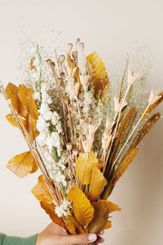 Idlewild Floral Co. - Golden Fall Market Bouquet: A hand holds a dried bouquet with autumn leaves, grasses, and blooms, perfect for lasting decorative beauty without maintenance.