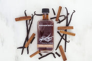 Runamok | Maple Syrups - Cinnamon + Vanilla Infused bottle, surrounded by vanilla sticks, highlighting its rich infusion, ideal for enhancing winter breakfasts or desserts.