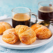 Nicola's Marketplace | Individual Mini Italian Sfogliatelle Pastries on a plate, dusted with powdered sugar, accompanied by espresso cups, highlighting their flaky layers and ricotta filling.