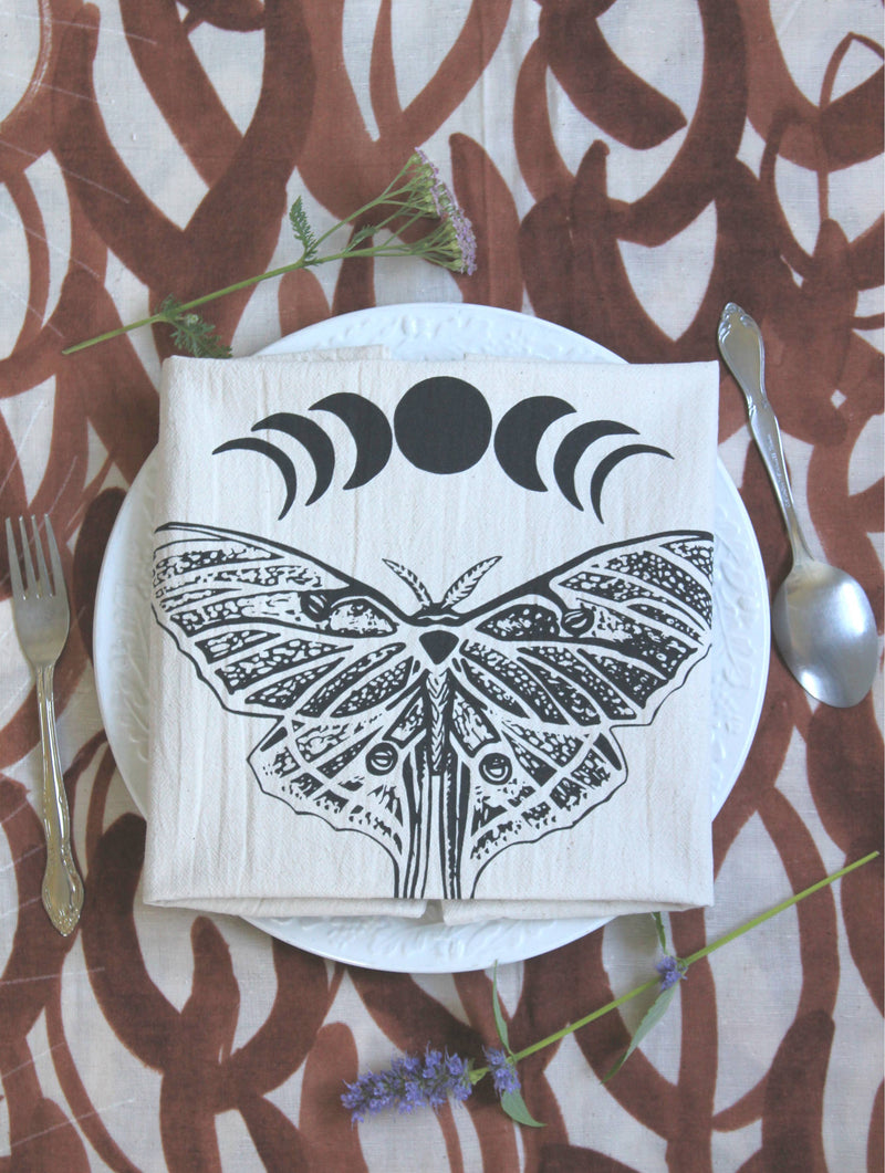 Hearth and Harrow - Organic Cotton Luna Moth Tea Towel with moon phases, elegantly set on a table, showcasing its eco-friendly design and fine dining appeal.