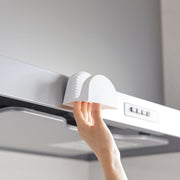 A hand attaches a Yamazaki Home Magnetic Pot Holder, Silicone, Black, to a range hood, ideal for hanging lightweight kitchen items.