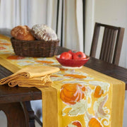 Caravan Home Pumpkin Orange/Mustard Runner adorns a dark wood table, featuring a pumpkin motif, with accompanying mustard napkins and a basket of bread.