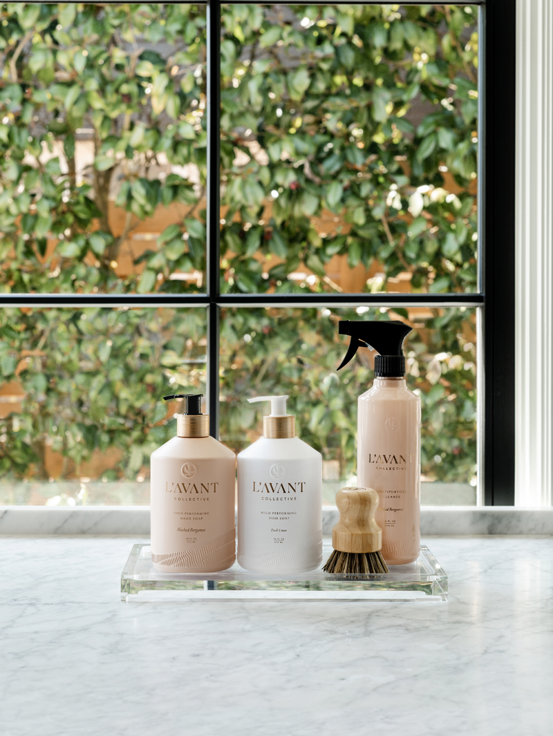L'AVANT Collective - High Performing Dish Soap - Blushed Bergamot in matte white glass bottles on a counter, highlighted among other cleaning essentials.