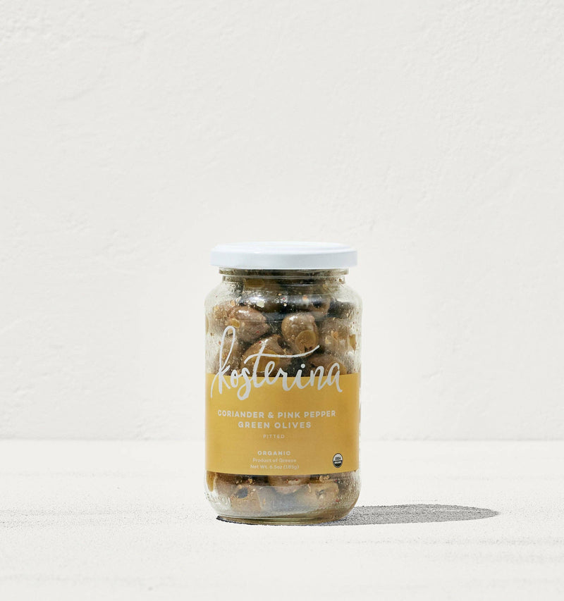 Kosterina - Coriander and Pink Pepper Green Olives in a jar, displayed on a white surface, showcasing handpicked Greek olives for salads or snacking.