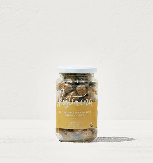 Kosterina - Coriander and Pink Pepper Green Olives in a jar, displayed on a white surface, showcasing handpicked Greek olives for salads or snacking.