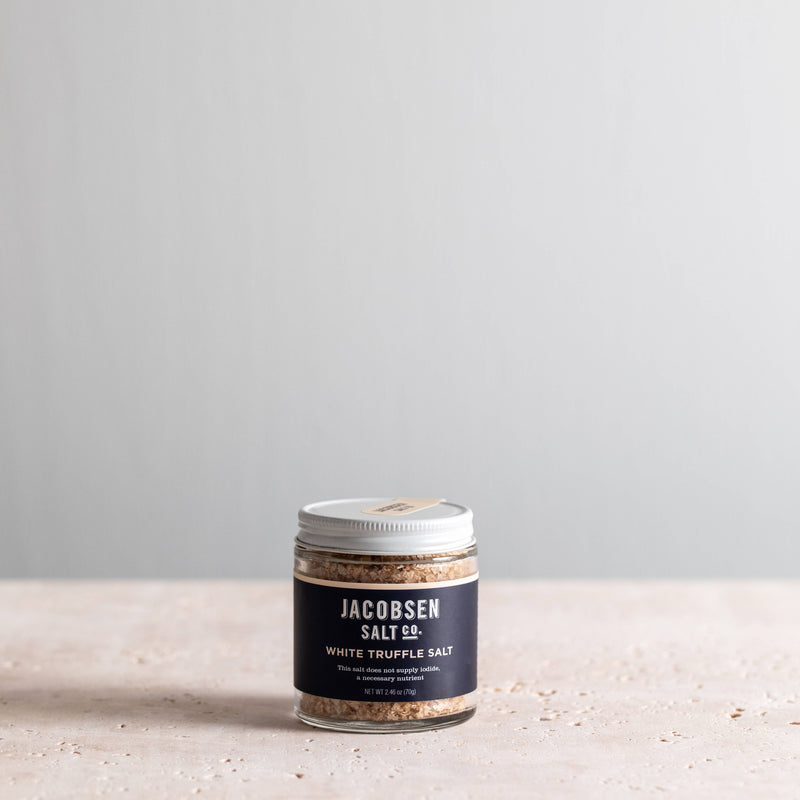 Jacobsen Salt Co. - White Truffle Salt in a clear jar with silver lid, showcasing coarse salt and truffle pieces, perfect for enhancing gourmet dishes.
