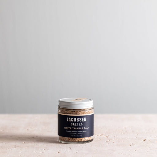 Jacobsen Salt Co. - White Truffle Salt in a clear jar with silver lid, showcasing coarse salt and truffle pieces, perfect for enhancing gourmet dishes.