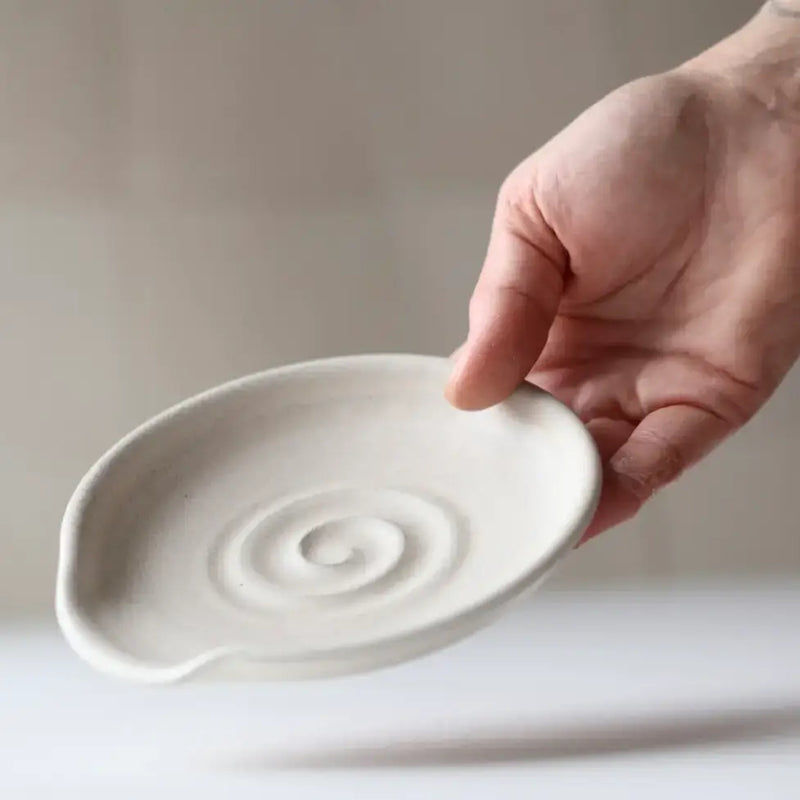 Hand holding Gravesco Pottery handmade ceramic spoon rest with raised spiral design, ideal for stovetop utensil rest.