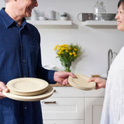 People exchanging bambu® - Disposable Bamboo Round Plates: 11 inches in a modern kitchen, highlighting eco-friendly, stylish, compostable dining options from Athens Cooks.