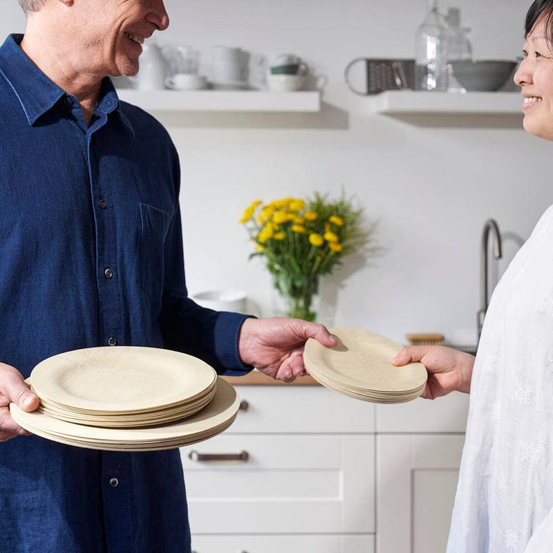 People exchanging bambu® - Disposable Bamboo Round Plates: 11 inches in a modern kitchen, highlighting eco-friendly, stylish, compostable dining options from Athens Cooks.