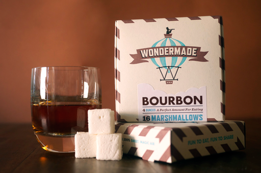 Wondermade - Bourbon Marshmallows next to a lowball glass of bourbon whisky, showcasing two branded boxes, highlighting their sweet, non-alcoholic flavor made with real cane sugar.