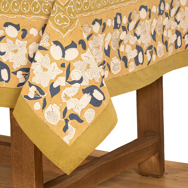 Couleur Nature - Forest Harvest Mustard & Blue tablecloth featuring a hand-printed fruit and foliage motif, highlighting Provencal charm on a wooden table corner.