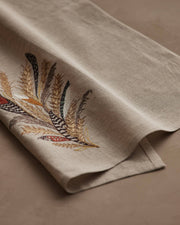 Coral & Tusk - Wheat Harvest Tea Towel features embroidered feathers and wheat in earthy tones on natural linen, perfect for seasonal kitchen decor.