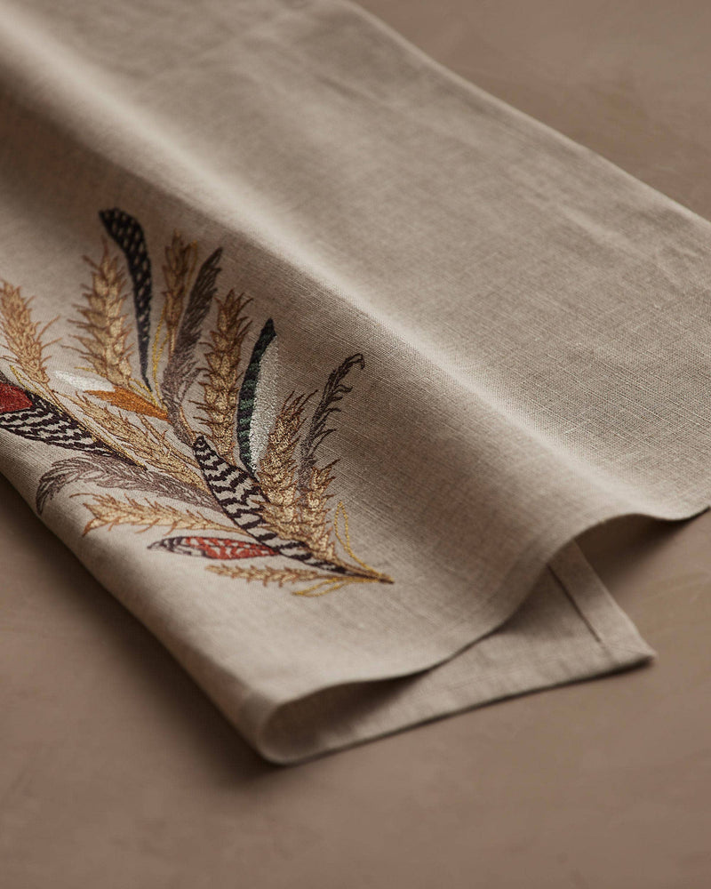 Coral & Tusk - Wheat Harvest Tea Towel features embroidered feathers and wheat in earthy tones on natural linen, perfect for seasonal kitchen decor.