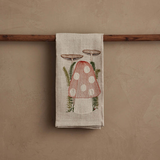 Coral & Tusk - Mushroom Tea Towel with embroidered toadstool and ferns on natural linen, draped over a wooden rod. Perfect for adding whimsy to your kitchen.