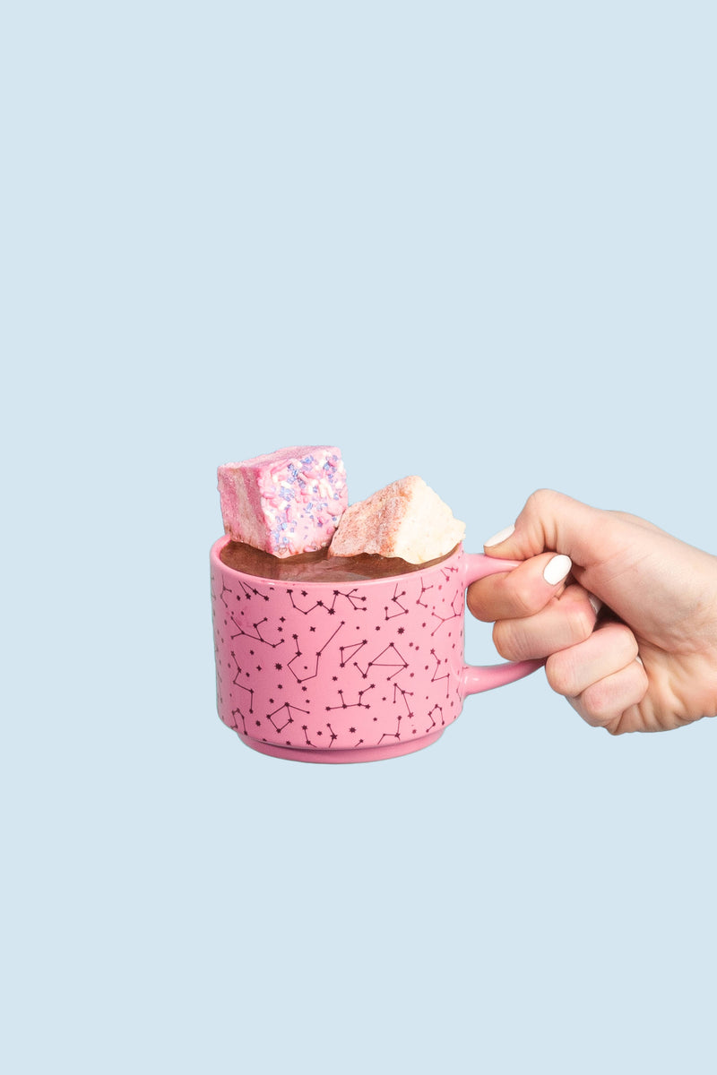 Hand holding a pink ceramic mug with Malvi Mallow - Cotton Candy 4-Pack Marshmallows, featuring pink and off-white marshmallows atop a dark beverage.