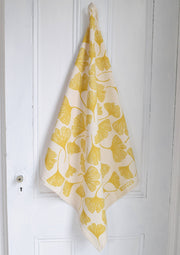 Hearth and Harrow - Ginkgo Leaf Tea Towel - Organic Cotton - Oversized 30 x 30, featuring stylized yellow ginkgo leaves, hanging from a white door knob.