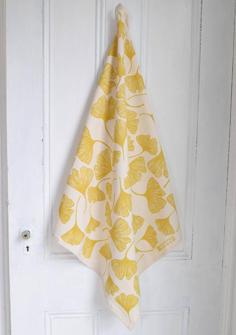 Hearth and Harrow - Ginkgo Leaf Tea Towel - Organic Cotton - Oversized 30 x 30, featuring stylized yellow ginkgo leaves, hanging from a white door knob.