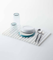 Yamazaki Home - Tower Folding Dish Drainer Mat with inverted glasses, plates, spoon, and fork, showcasing its drying functionality and space-saving design.