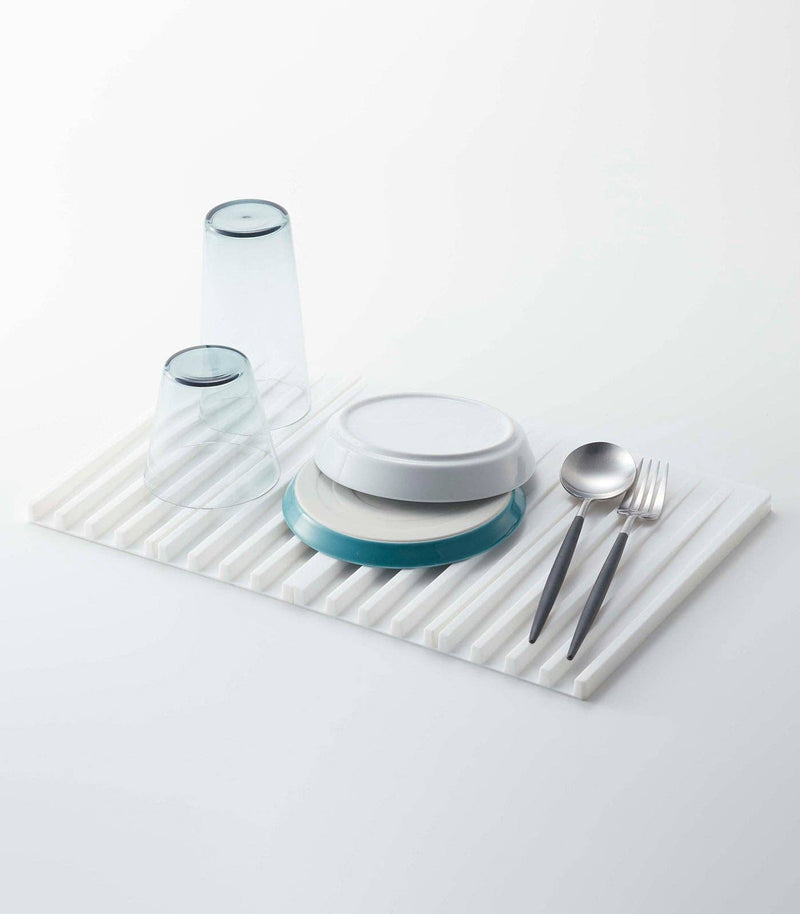 Yamazaki Home - Tower Folding Dish Drainer Mat with inverted glasses, plates, spoon, and fork, showcasing its drying functionality and space-saving design.