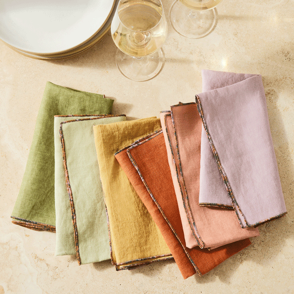 Atelier Saucier | Mix-and-Match Chroma Napkins, Set of 6, displayed in warm hues with ombre edging, alongside ceramic plates and wine glasses on a stone surface.