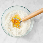 King Arthur Baking Company | Baker's Batter Whisk with a triple-loop design, resting beside a bowl of flour, ideal for mixing batters seamlessly.