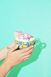 Hands hold a teacup filled with whipped cream, showcasing Malvi Mallow - Cotton Candy 4-Pack Marshmallow, topped with sprinkles and a pink marshmallow cube.