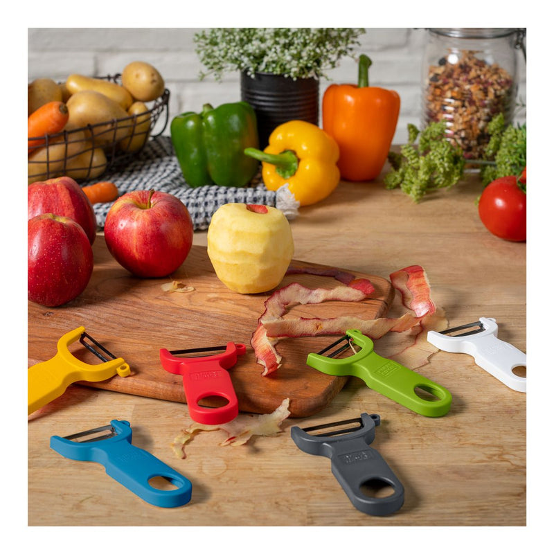 Kuhn Rikon | Original Swiss Peeler, Yellow, lies among colorful peelers and fresh produce, showcasing its sharp carbon steel blade on a wooden countertop.