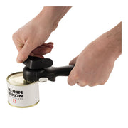 Hands using Kuhn Rikon LidLifter, Black, effortlessly open a tin can, showcasing its self-attaching design and safety features, ideal for kitchen enthusiasts.