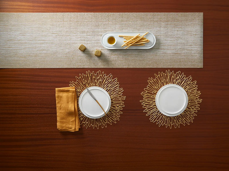 Chilewich | Bloom Placemats - Gilded on a dining table, elegantly displaying intricate openwork design, complementing a sophisticated table setting with plates and bread sticks.