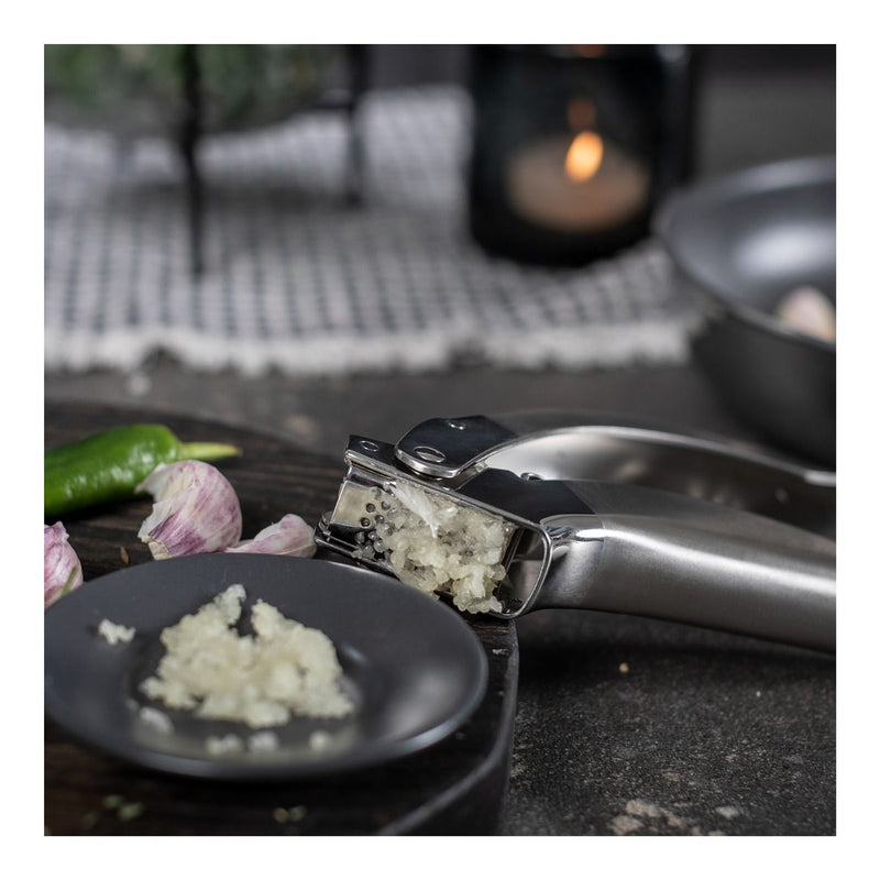 Kuhn Rikon | Epicurean Garlic Press effortlessly crushes garlic into a dish, showcasing its ergonomic, stainless-steel design with a convenient pullout sieve for easy cleaning.