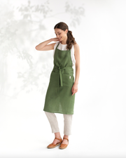 Woman wearing MagicLinen - Charcoal Grey Linen Bib Apron with Pockets, standing and smiling, highlighting its stylish functionality for cooking or gardening.
