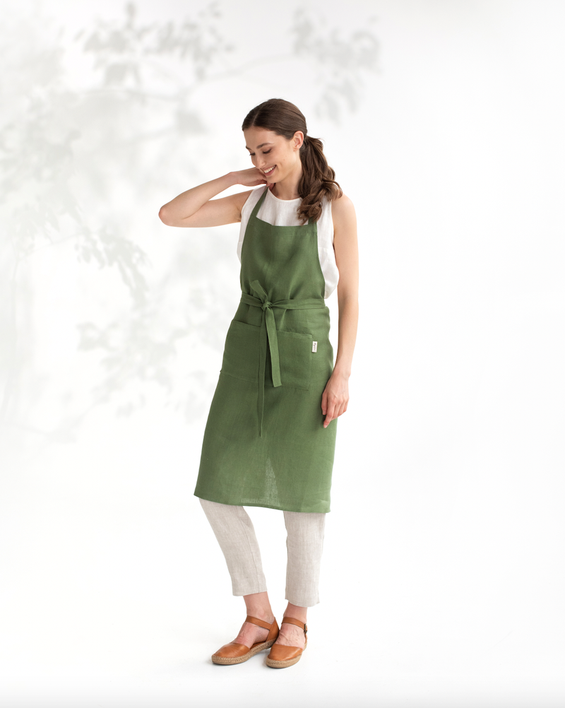 Woman wearing MagicLinen - Charcoal Grey Linen Bib Apron with Pockets, standing and smiling, highlighting its stylish functionality for cooking or gardening.