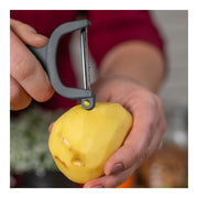 Person using the Kuhn Rikon | Original Swiss Peeler - Grey to peel a potato, highlighting its razor-sharp carbon steel blades and ergonomic design for efficient handling.