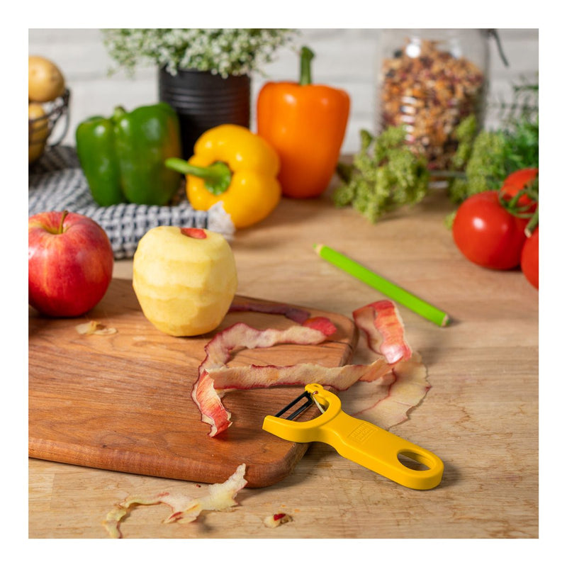 Kuhn Rikon | Original Swiss Peeler, Yellow, on cutting board with apple peels, showcasing ergonomic design and razor-sharp carbon steel blades for efficient fruit and vegetable preparation.