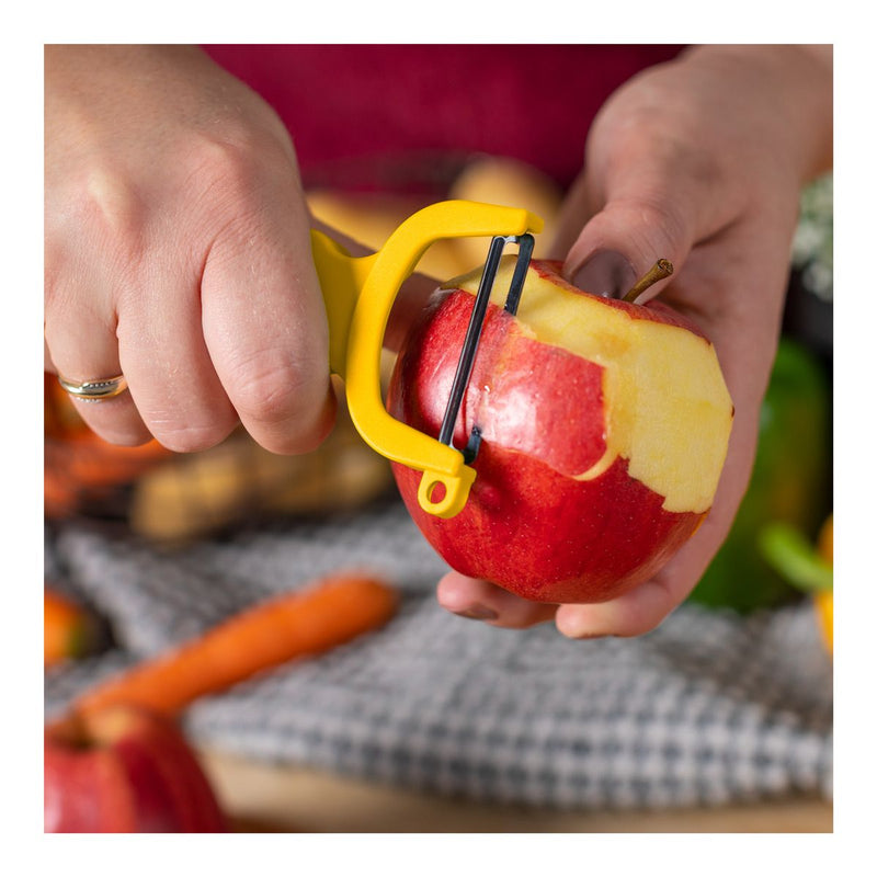 Hands using Kuhn Rikon | Original Swiss Peeler, Yellow, effortlessly removing apple skin, showcasing its ergonomic design and sharp carbon steel blade.