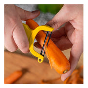 Close-up of a Kuhn Rikon | Original Swiss Peeler, Yellow, effortlessly peeling a carrot with its sharp carbon steel blade, showcasing its ergonomic design.