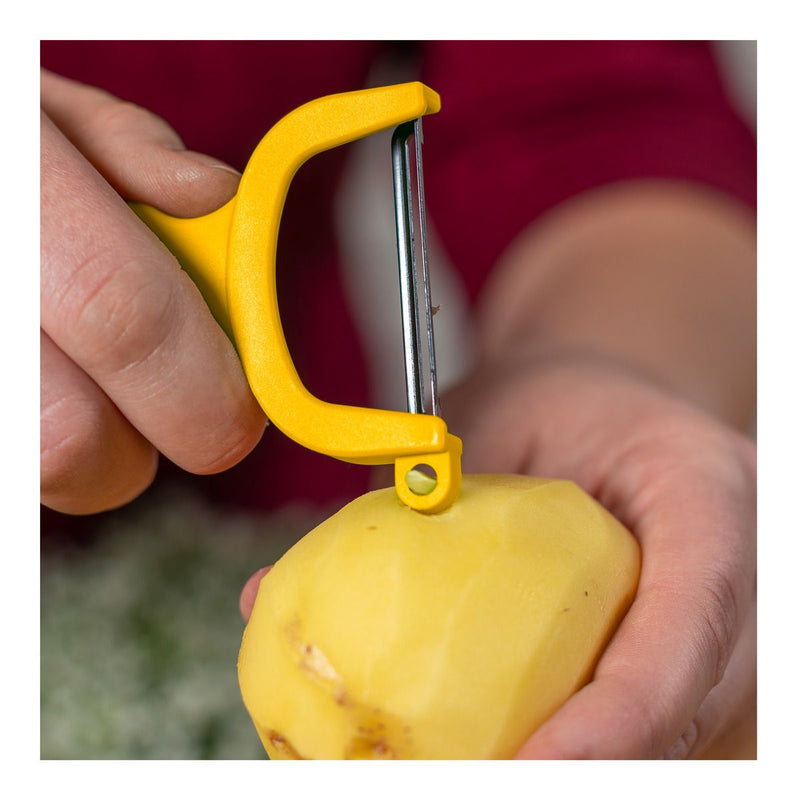A person uses the Kuhn Rikon | Original Swiss Peeler, Yellow, to peel a potato, showcasing its razor-sharp carbon steel blade effortlessly removing the skin.